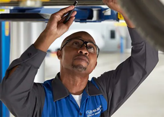 A Subaru technician under a Subaru vehicle